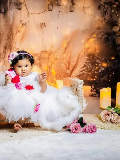 A sweet portrait of the baby girl sitting comfortably on the miniature bed, surrounded by warm, glowing lights.