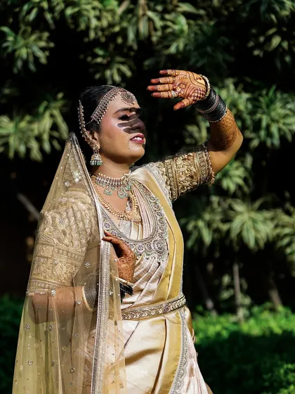 An artistic outdoor portrait of a bride in a golden saree, using the harsh sunlight to create dramatic shadows and a high-fashion look.