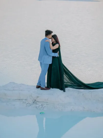 A romantic embrace on a ledge overlooking the water. The reflection of the couple and the sky in the calm water creates a beautiful, serene, and almost magical effect.