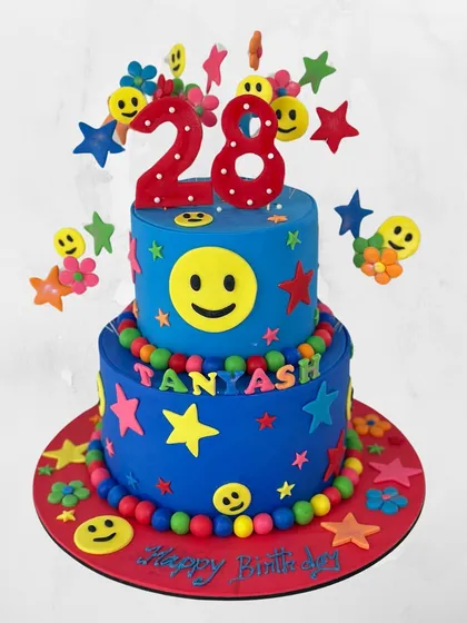 This two-tiered cake is all about spreading smiles. The bright blue design is covered in cheerful smiley faces, stars, and colorful details for a happy 28th birthday.