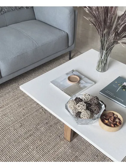 A styled coffee table vignette. A mix of books, natural decorative objects, and dried grasses on a clean white tabletop creates a look that is both minimalist and warm.