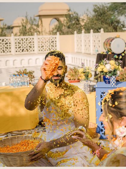 A playful moment during the Haldi ceremony, where the groom is covered in turmeric paste and flower petals, captured in a fun, candid shot.