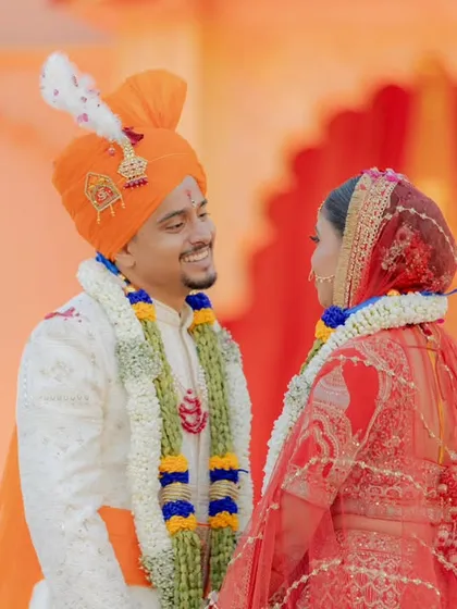 A sweet, candid moment of the couple looking at each other right after the varmala. The red backdrop adds to the richness of the scene.