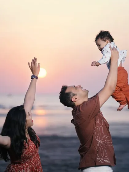 A candid and joyful family photo on the beach at sunset. The action of tossing the baby in the air adds a sense of fun and spontaneity to this beautiful memory.