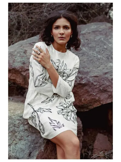 A black and white shot from a creative editorial. The focus is on the texture and pattern of this sequined floral dress, with the model's pose creating a sense of quiet introspection against the rocky landscape.