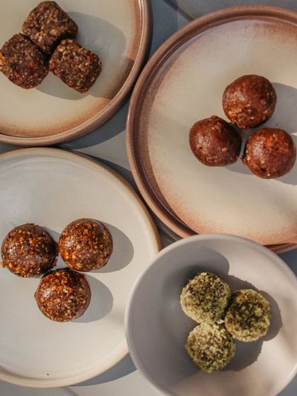 Our healthy energy balls are the perfect guilt-free treat. This overhead shot shows the variety we offer, including rose cardamom cubes, snicker bites, bliss balls, and matcha protein balls.