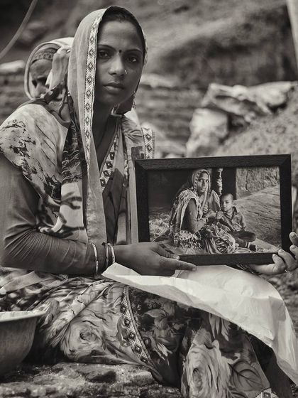 A woman holds a framed photograph of what appears to be herself and her child from an earlier time. This image within an image is a powerful story of memory, identity, and the passage of time.