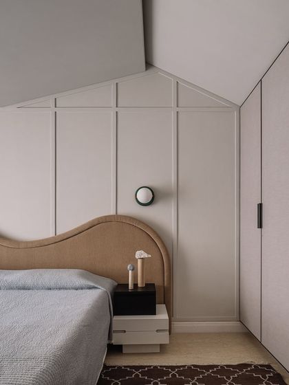 The guest bedroom features a unique design where the headboard and wall paneling become one architectural element. This approach blurs the lines between furniture and structure, creating a cohesive and artful space.