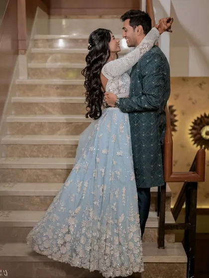 An elegant, full-length portrait that showcases how we guide couples into poses that feel natural and romantic. The soft lighting on the staircase highlights the intricate details of the bride's powder blue lehenga and the groom's coordinating sherwani.