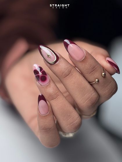 A close-up on the hand-painted abstract floral and gold-rimmed accent nail. The combination of deep red, pink, and gold is elegant and modern.