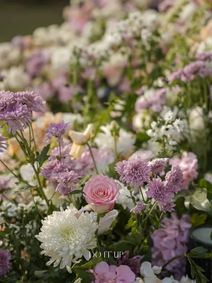 A dreamy close-up of a floral arrangement from a Jaipur wedding. The soft focus highlights a delicate pink rose nestled among a bed of white and lavender chrysanthemums.