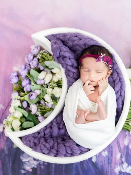 A peacefully sleeping newborn nestled in a celestial moon prop, surrounded by delicate purple and white flowers. This image showcases one of our many creative and safe newborn photography themes.