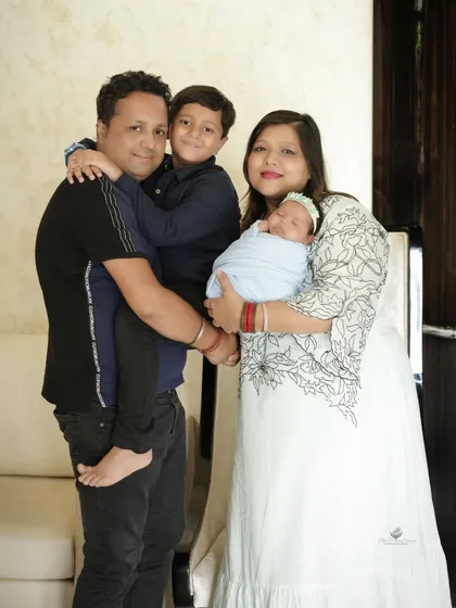 A joyful standing portrait of a family of four. The father holds the older son, while the mother cradles the newborn, showcasing a happy and complete family unit.