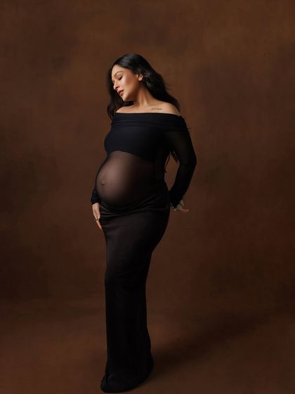 A serene and beautiful portrait in a sheer black off-the-shoulder gown, against a rich brown backdrop.