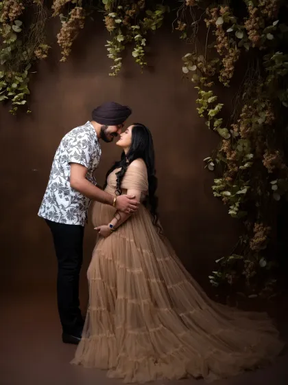 A romantic kiss shared between the parents-to-be. This full-length portrait showcases their connection amidst a backdrop of hanging vines and flowers.