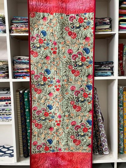 A long table runner featuring a beautiful floral print and solid red ends.