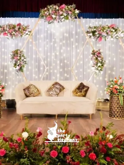 This wedding reception stage was designed for pure romance. A backdrop of twinkling fairy lights, a modern geometric frame adorned with pink and red floral arrangements, and an elegant velvet sofa created a beautiful focal point for the happy couple.