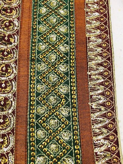 A rich and opulent saree border featuring intricate sequin and zari work in green, maroon, and gold. This heavy designer lace is ideal for bridal wear and special occasion outfits.