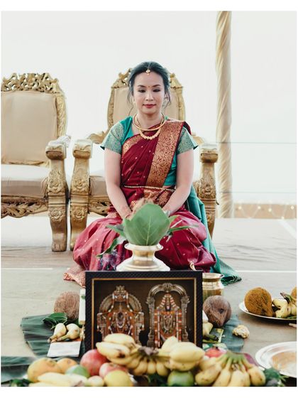 The bride sits gracefully during a puja at her South Indian wedding, surrounded by traditional offerings. A moment of peace and devotion.