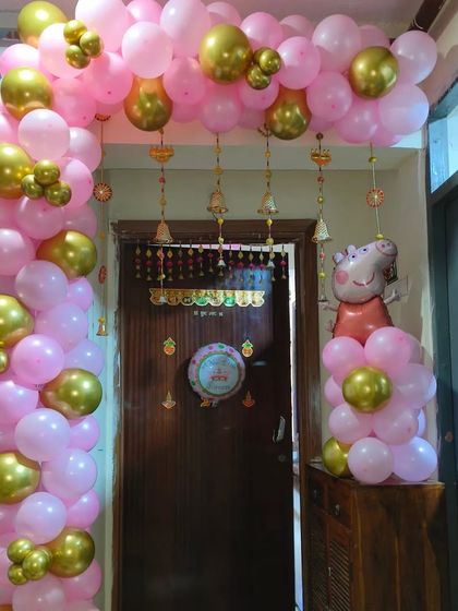 I can mix modern characters with traditional touches for kids' events. This entrance features a pink and gold balloon arch with a Peppa Pig foil balloon, complemented by traditional Indian bell hangings for a unique fusion look.