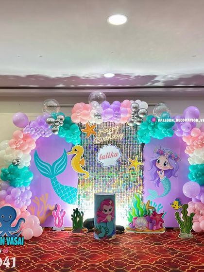 A grand mermaid theme for Lalita's first birthday. This stage setup includes a shimmer backdrop, character cutouts, and a pastel balloon arrangement.