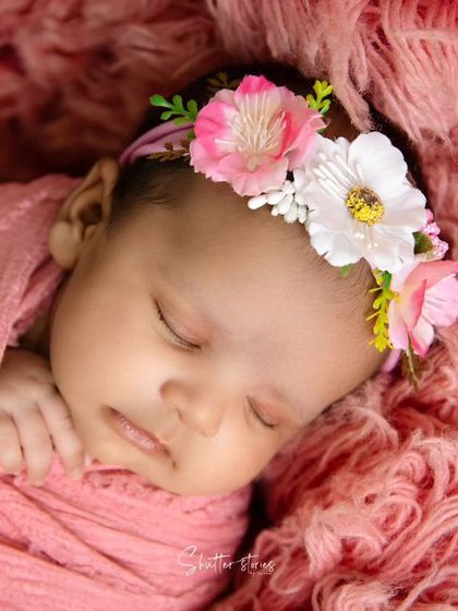 A close-up of the pink-swaddled newborn, showing the details of her floral headband.