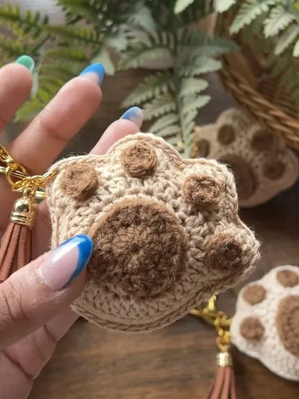 A detailed close-up of the crochet paw keychain. The texture is soft yet durable, and it comes with a tassel and a sturdy gold-tone clasp.
