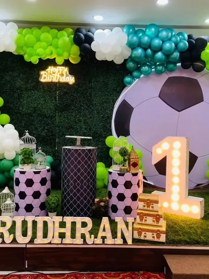 For the little sports fan, this is a football-themed first birthday backdrop. It includes a grass-like turf floor, a large football prop, a balloon garland in team colors, and custom-themed cake stands.