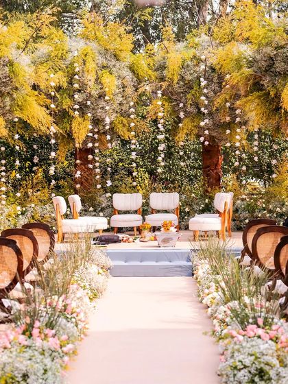 A beautiful daytime wedding mandap setup in a garden, with lush yellow foliage and hanging floral strings.