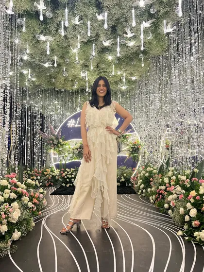 Posing at a beautifully decorated event. The whimsical decor with hanging crystals and flowers perfectly complements the playful ruffles of my outfit.