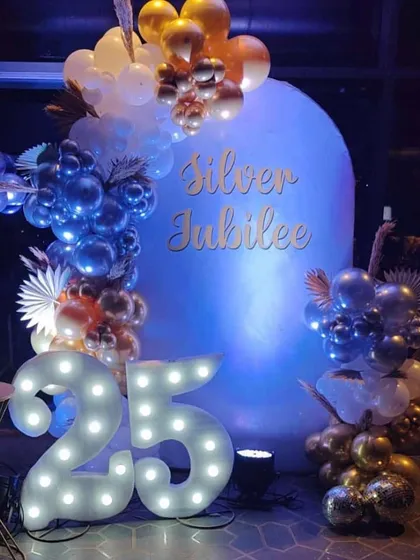 Celebrating a silver jubilee with a stunning blue, silver, and gold balloon arrangement. The large marquee numbers and custom "Silver Jubilee" sign make it a perfect photo spot.