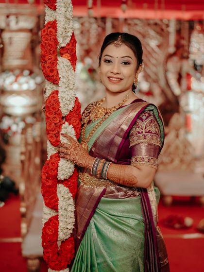 A beautiful portrait of a bride in a light green saree, posing next to a floral arrangement.