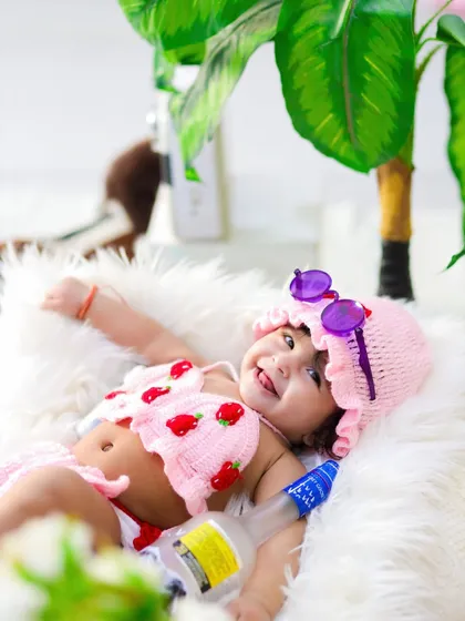 A six-month-old baby girl in a hand-knitted strawberry bikini, lounging on a fur rug for her beach-themed milestone shoot.