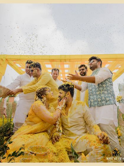 A moment of playful affection as the bride applies Haldi to the groom, surrounded by their cheering friends.