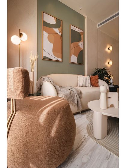 Sunlight streams into the living space, highlighting the warm, earthy tones of the furniture and decor. The combination of a sage green accent wall and terracotta-colored art adds a gentle touch of color to the otherwise neutral palette.