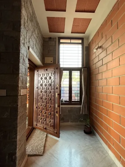 A hallway where a rugged stone wall meets a smooth brick wall, with an intricately carved wooden door adding a touch of tradition.