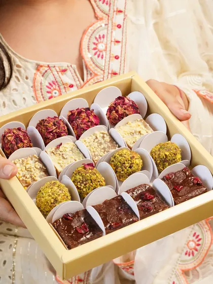 A box of assorted festive sweets being held out as a gift, showcasing the beautiful variety of mithai.