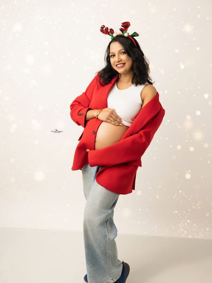 A happy and bright solo portrait from a Christmas session. The mother-to-be wears reindeer antlers and a festive red jacket, glowing with holiday spirit.