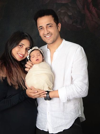 A beautiful family portrait with their newborn daughter. The parents are all smiles as they hold their swaddled baby, creating a memory they will always treasure.