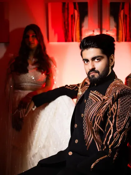 A stylish portrait of the groom from a cocktail event. The red lighting and his confident pose give this shot a bold, fashionable edge. The bride in the background adds a layer of romance.