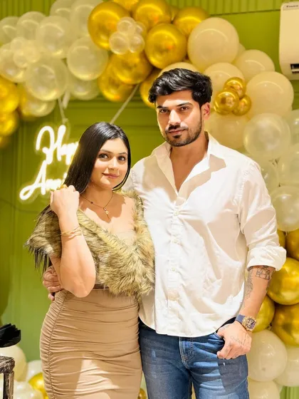 The couple posing for a photo in front of the gold and white balloon wall, a perfect memento of their special day.