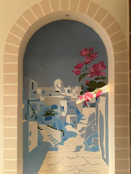 Adding the final touches of bougainvillea to the Santorini mural. The bright pink flowers bring life and vibrancy to the serene blue and white cityscape.