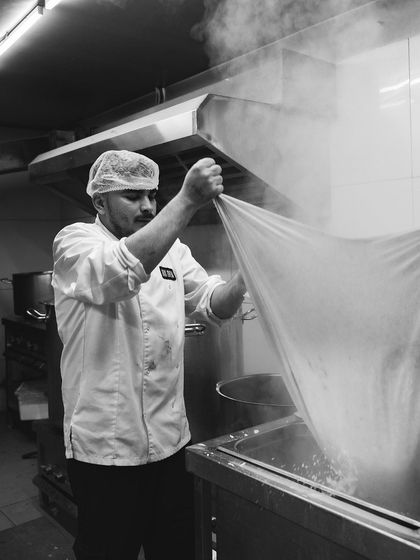 A black and white shot of a chef straining the cheese curds, capturing the traditional and labor-intensive nature of our craft.