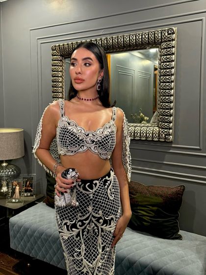 Reshma Arora radiates sheer elegance in our signature charcoal black pearl-embellished skirt and intricately designed bralette, elevated with a flowing cape.