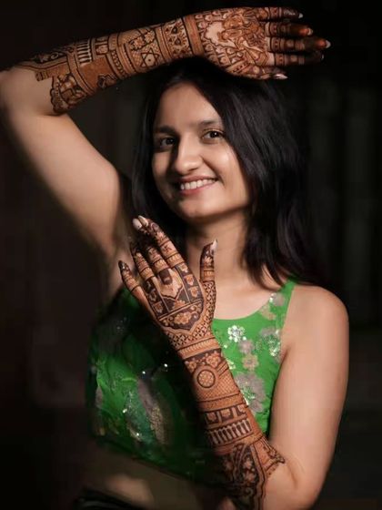 A happy bride posing with her full-arm back-hand mehandi. The design is intricate and covers her arms beautifully.