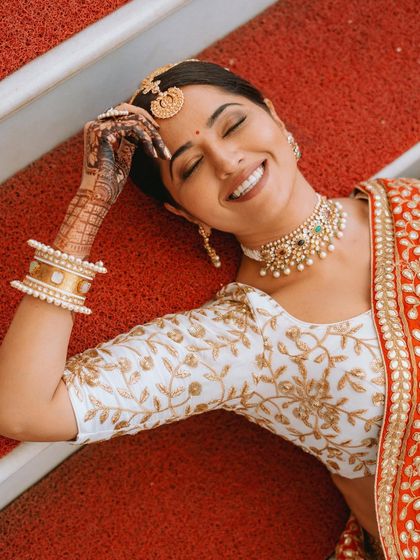 A creative overhead shot of the bride lying on a red carpet, her happy expression and beautiful attire creating a striking image.
