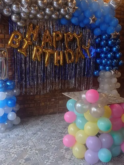 A first birthday decoration at a cafe in Dwarka. The setup includes a balloon wall with a shimmer curtain and a number '1' balloon pillar.