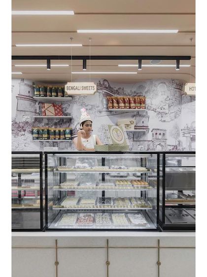 A view of the sweets counter, set against a custom wallpaper depicting the historic Gummanayaka fort. This artwork by Trupty Somaiah enriches the space with a strong sense of place and history.