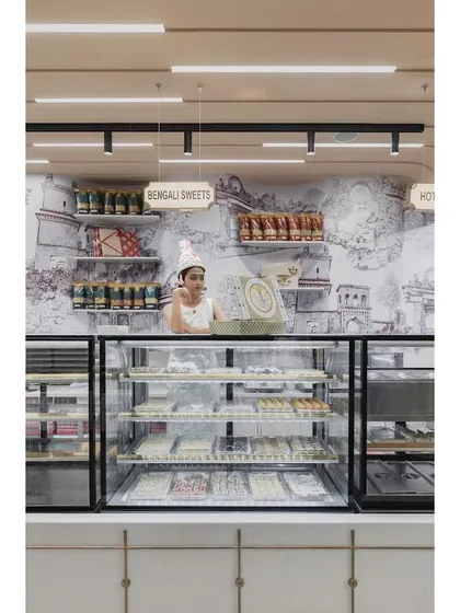A view of the sweets counter, set against a custom wallpaper depicting the historic Gummanayaka fort. This artwork by Trupty Somaiah enriches the space with a strong sense of place and history.