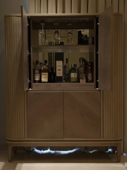 The hidden bar unit, open to display the collection. The mirrored back and glass shelves add depth and reflect light, making the interior feel spacious and bright.